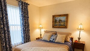 A bedroom with a bed, two bedside tables, a painting on the wall, and a window with curtains. - Vintage Charm-Modern Comfort•2BR/2BA home (Lovington)