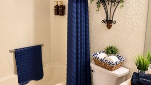 A bathroom with a bathtub, a toilet, a sink, a blue towel, and toiletries on the wall. - Vintage Charm-Modern Comfort•2BR/2BA home (Lovington)