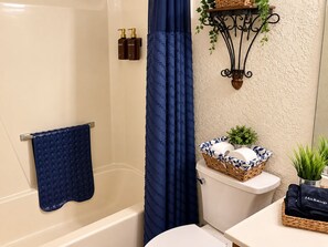 Ein Badezimmer mit einer Badewanne, einer Toilette, einem Waschbecken, einem blauen Handtuch und Pflegeprodukten an der Wand.