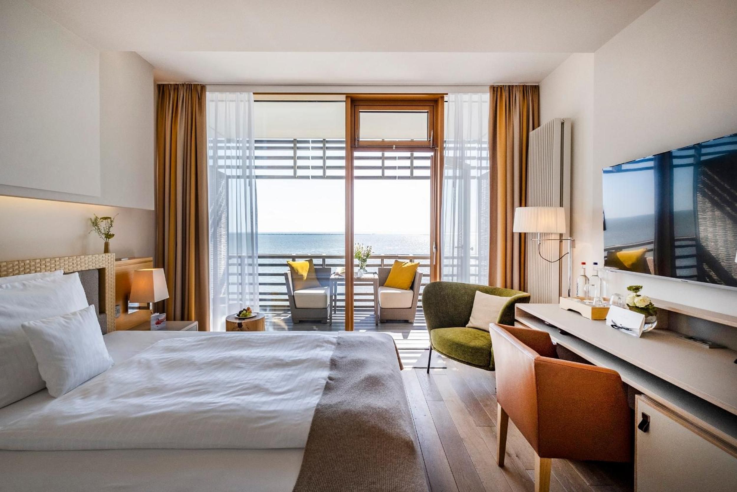 Ein Hotelzimmer mit einem grossen Bett, einem Schreibtisch mit Stuhl, einem Fernseher und einem Balkon mit Meerblick.