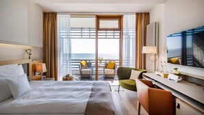 Ein Hotelzimmer mit einem grossen Bett, einem Schreibtisch mit Stuhl, einem Fernseher und einem Balkon mit Meerblick.