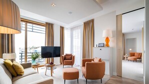 Ein modernes Hotelzimmer mit Flachbildfernseher, zwei Sesseln, einer Couch, einem Couchtisch und einem Essbereich mit einer Lampe.