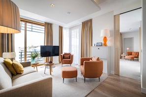 A modern hotel room with a flat-screen TV, two armchairs, a sofa, a coffee table, and a dining area with a lamp. - Budersand (Hörnum (Sylt))