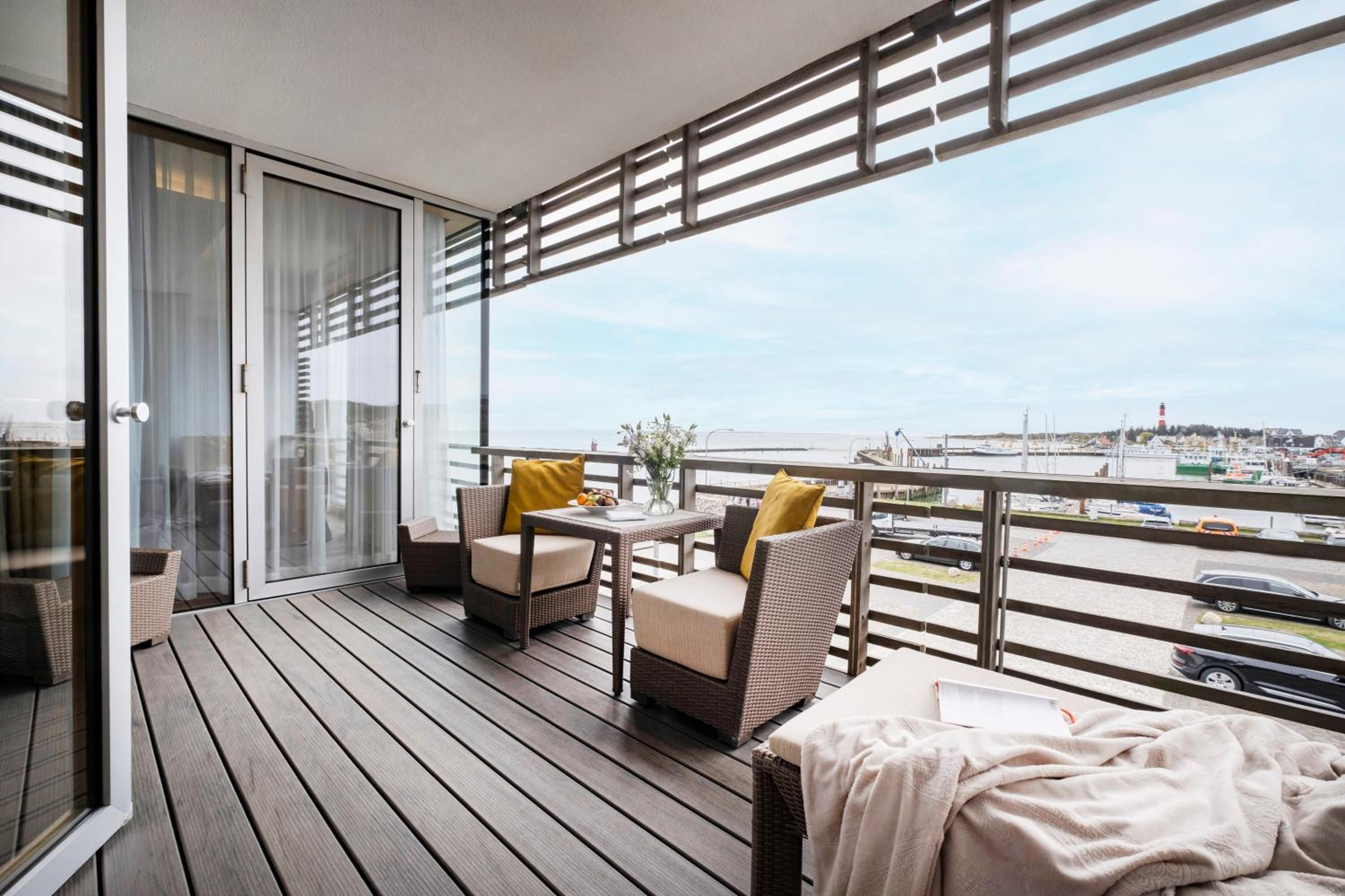 Ein Balkon mit Korbmöbeln, einem Tisch und Blick auf einen Yachthafen.