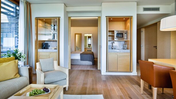 Ein modernes Interieur mit einer Couch, einem Esstisch, einer Küchenzeile und einem Schlafzimmer mit Bett und Spiegel.