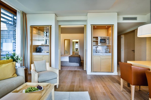 A modern interior with a sofa, a dining table, a kitchen area, and a bedroom with a bed and a mirror. - Budersand (Hörnum (Sylt))