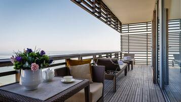 Ein Balkon mit Korbmöbeln, einem Tisch mit Blumen und Blick aufs Meer.
