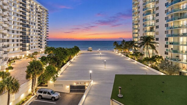 A multi-story hotel with a parking area, a pool, and a view of the ocean at sunset. - Oceanfront Luxury | 2BR Condo| No Resort Fees (Hollywood)