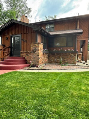 A two-story house with a brick facade, a front porch with steps, and a small garden area.
