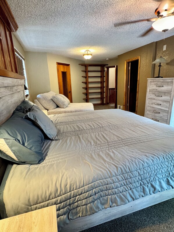 A bedroom with a large bed, a wooden headboard, a ceiling fan, and a dresser.