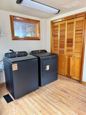 A laundry room with two Whirlpool washers, a wooden closet, and a window above the washers.