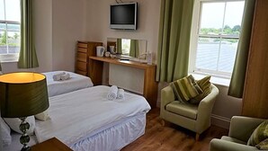Habitación de hotel con dos camas, un televisor, un escritorio con espejo, una silla y una ventana con cortinas.