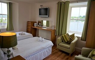 Habitación de hotel con dos camas, un televisor, un escritorio con espejo, una silla y una ventana con cortinas.
