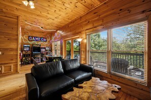 A wooden cabin interior with a black leather sofa, wooden tables, and arcade games. - Mountain Views, Four King Bedrooms, Hot Tub, Pool, Game Room &( EV Charger) (Pigeon Forge)