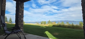 Eine Steinterrasse mit Blick auf eine grüne Rasenfläche und ein Gewässer in der Ferne.