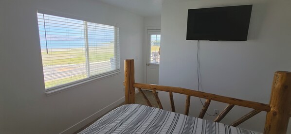 Ein Zimmer mit einem Bett, einem Fenster mit Jalousien, einer Tür und einem an der Wand befestigten Fernseher.