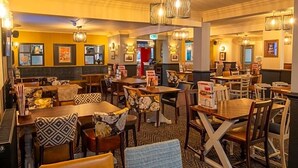 A restaurant with multiple dining tables and chairs, some with patterned cushions. - Charnwood Arms by Good Night Inns (Coalville)
