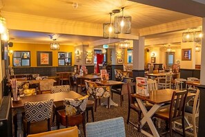 Ein Restaurant mit mehreren Tischen und Stühlen, einige davon mit gemusterten Kissen.