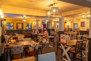 Un restaurante con varias mesas y sillas, algunas con cojines estampados.
