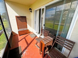 Ein Balkon mit Holzmöbeln, einer Schiebeglastür und einer kleinen Außenfläche mit Fußmatte.