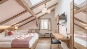 Une chambre mansardée chaleureuse avec un plafond en pente, des poutres en bois, un lit, un bureau et un téléviseur.