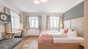 Une chambre d’hôtel avec un lit, un bureau, une chaise, une télévision et deux fenêtres.
