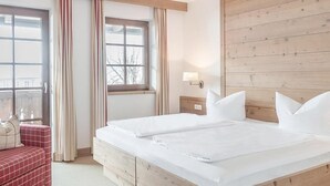 Une chambre d’hôtel avec un grand lit, une tête de lit en bois, une fenêtre avec des rideaux, une table de chevet avec une lampe et un canapé rouge à carreaux.
