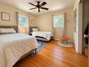 A bedroom with two beds, a ceiling fan, a small table, and a window with curtains.