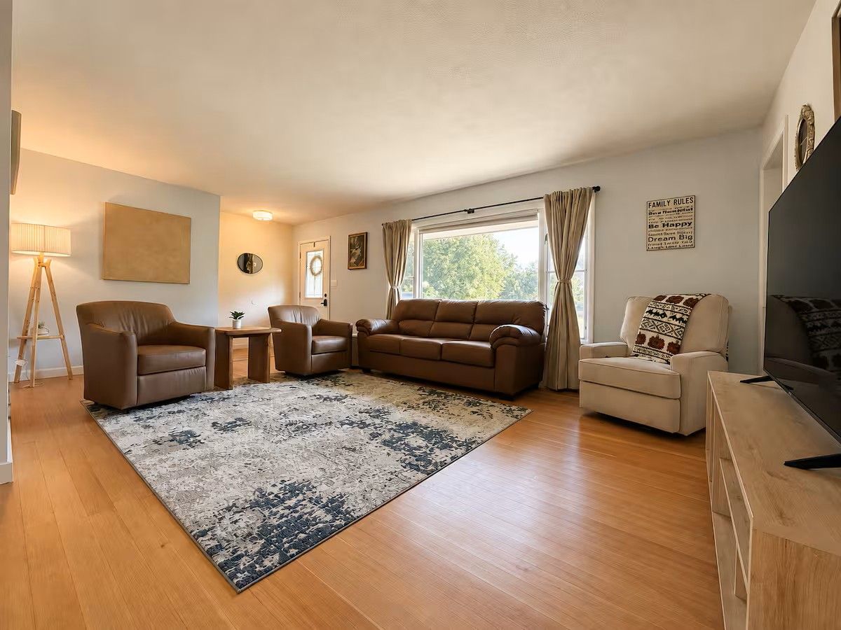 Un salon comprenant un canapé, des fauteuils, une table basse, un téléviseur et une grande fenêtre.