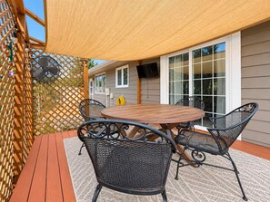 An outdoor patio with a round wooden table and four chairs, a yellow shade, and a lattice fence.