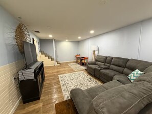 A living room with a sectional sofa, a fireplace, a staircase, and a dining area.