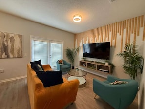 A living room with a sofa, armchairs, a coffee table, a flat-screen TV, and a bamboo wall panel. - 8947 SD - 4BR Home in West Lucaya | Near Disney (Kissimmee)