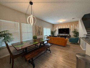 A modern living room with a wooden dining table, benches, a sofa, and a television. - 8947 SD - 4BR Home in West Lucaya | Near Disney (Kissimmee)