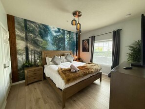 A bedroom with a wooden bed, a nightstand, a wall mural, a ceiling light fixture, and a window with curtains. - 8947 SD - 4BR Home in West Lucaya | Near Disney (Kissimmee)