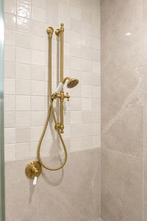 A bathroom with a gold shower system, white tiled walls, and a beige floor. - Buddina Boutique Coastal Studio on the Waterfront (Buddina)