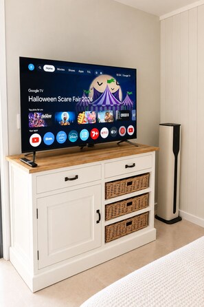 Un téléviseur posé sur un meuble blanc, avec une télécommande, affichant une interface Google TV sur le thème d’Halloween.