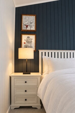 A bedroom with a white bed, a nightstand with a lamp, and two framed artworks on the wall. - Buddina Boutique Coastal Studio on the Waterfront (Buddina)