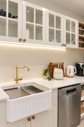 A modern kitchen with white cabinetry, a stainless steel sink, a gold faucet, a coffee maker, and a dishwasher. - Buddina Boutique Coastal Studio on the Waterfront (Buddina)