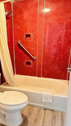 A bathroom with a red tiled wall, a white toilet, and a bathtub with a towel. - Your Place to stay! Big SEC Clash 1 Bedroom King Bed. Dreamland Inn in Senatobia (Senatobia)