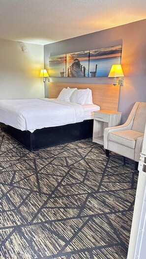 A hotel room with a bed, a chair, a desk, and a wall-mounted lamp. - Your Place to stay! Big SEC Clash 1 Bedroom King Bed. Dreamland Inn in Senatobia (Senatobia)