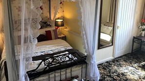 Ein Himmelsbett mit Baldachin, ein Nachttisch mit Lampe, ein Spiegel und eine Tür.