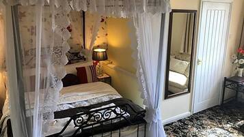 Una cama con dosel y cuatro columnas, una mesita de noche con lámpara, un espejo y una puerta.