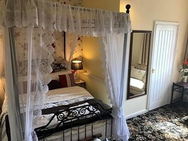 Una cama con dosel y cuatro columnas, una mesita de noche con lámpara, un espejo y una puerta.