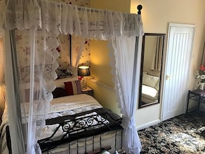 A four-poster bed with a canopy, a bedside table with a lamp, a mirror, and a door. - Englands Rose Pub (Thame)