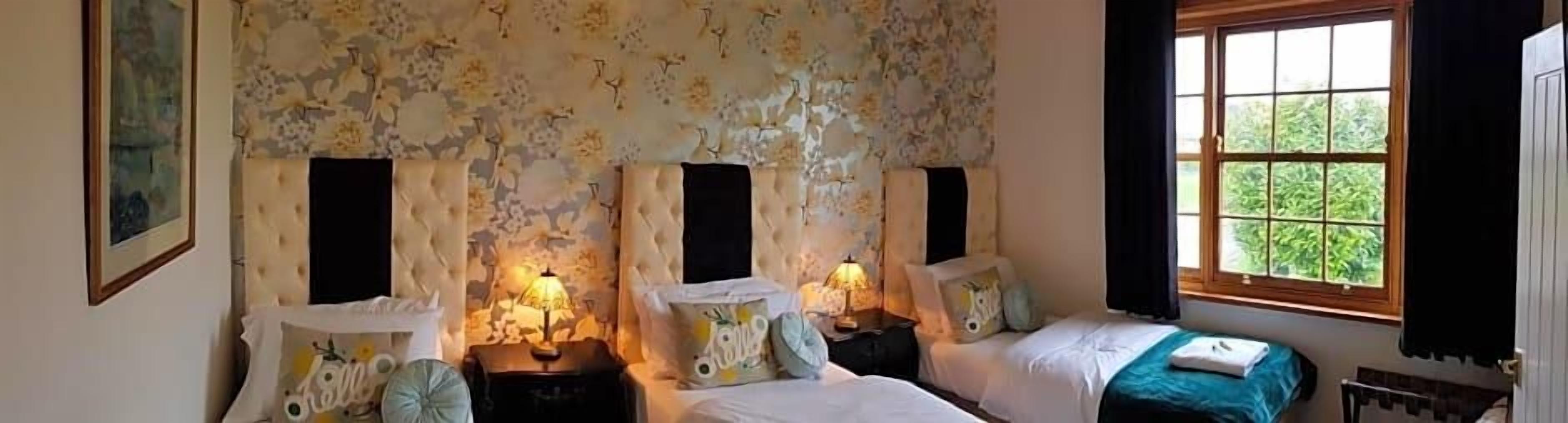 Un dormitorio con dos camas, papel tapiz floral y una ventana con cortinas.