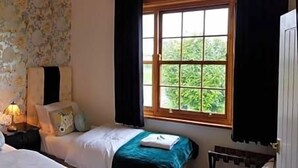 Ein Schlafzimmer mit zwei Betten, floralem Wandpapier und einem Fenster mit Vorhängen.