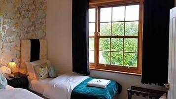 Un dormitorio con dos camas, papel tapiz floral y una ventana con cortinas.