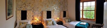 Un dormitorio con dos camas, papel tapiz floral y una ventana con cortinas.