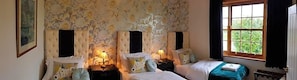 A bedroom with two beds, a floral wallpaper, and a window with curtains. - Englands Rose Pub (Thame)