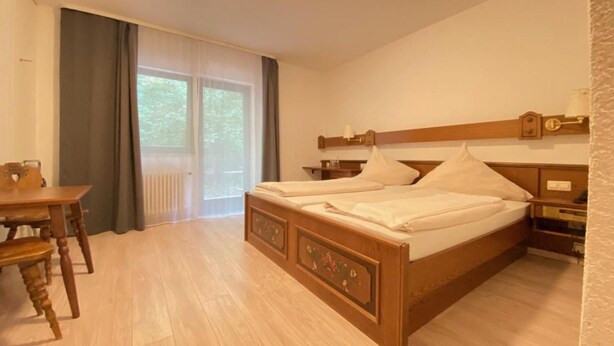 A bedroom with a wooden bed, a wooden desk, and a window with curtains. - Alemannenhof Engel (Rickenbach)